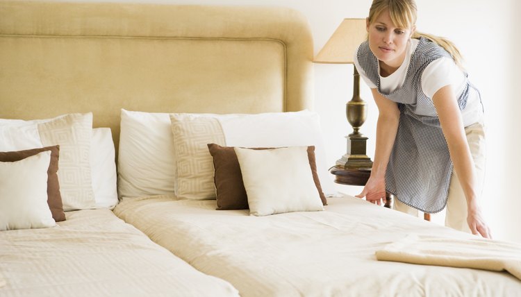 Maid making bed in hotel room
