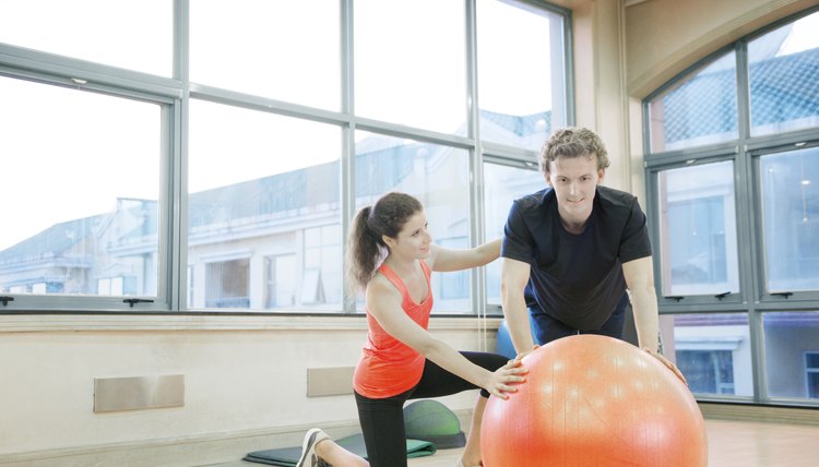 Trainer helping young man with exercises on fitness ball