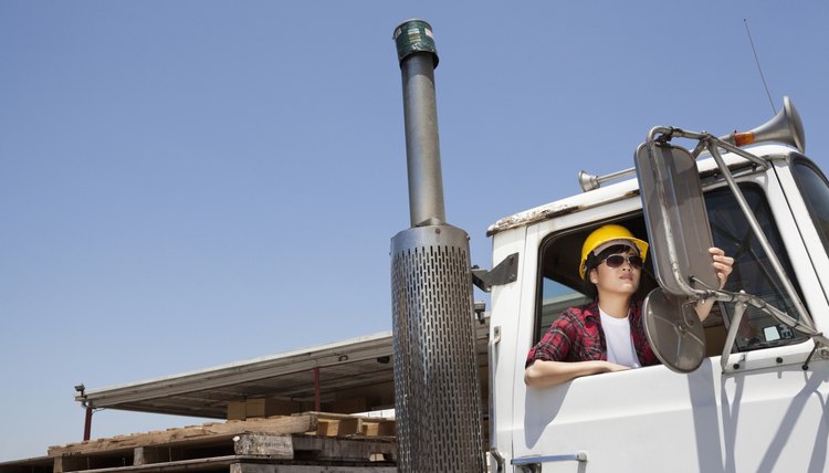Female industrial worker adjusting mirror while sitting in logging truck