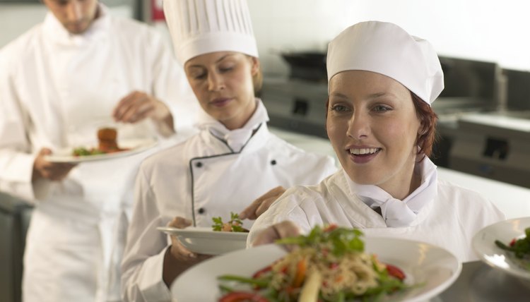 Three chefs holding dishes in kitchen (focus on young woman smiling)