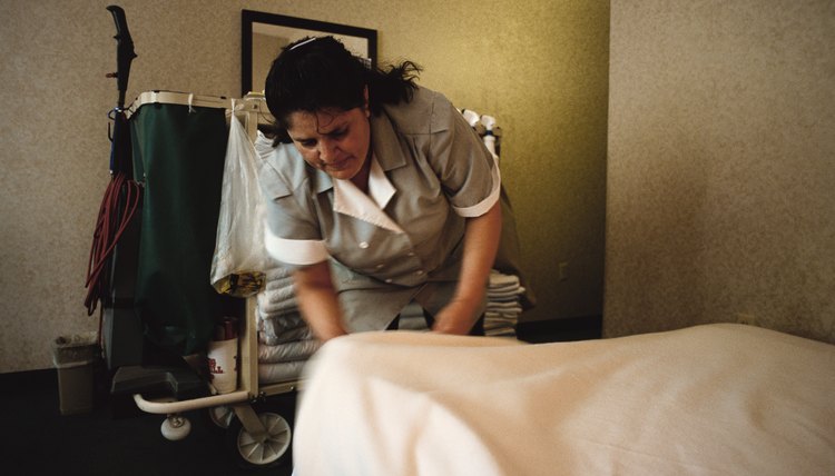a hispanic woman at a hotel room tucks bedsheets into a bed