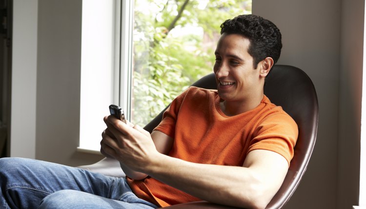 Latino man text-messaging at home by window