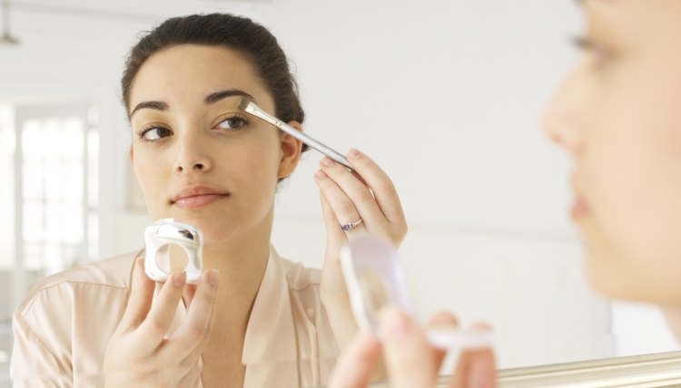 Young woman applying make-up in mirror, using brush, close-up