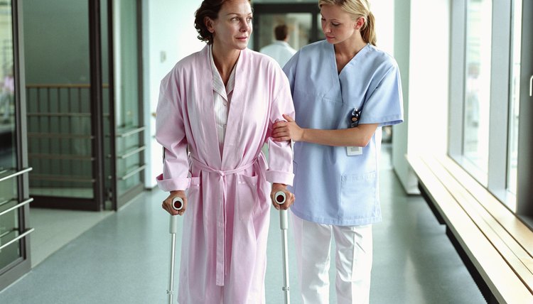 Female nurse holding patient using crutches in hospital corridor