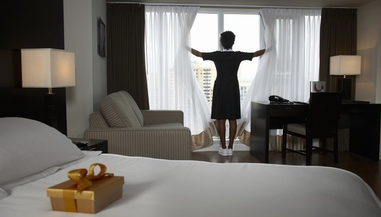 Chambermaid opening curtains, box of chocolates on guest's bed