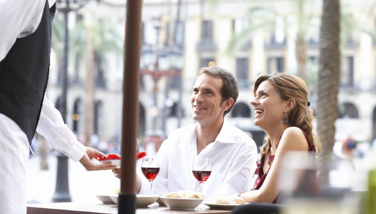 Waiter bringing food to couple at table in restaurant