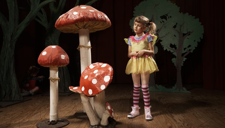 Girl (5-7) standing beside giant toadstools on stage