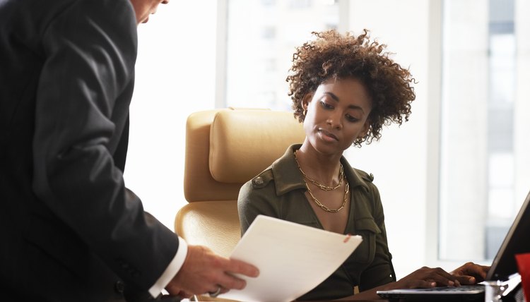Businessman on businesswoman's desk looking at paperwork