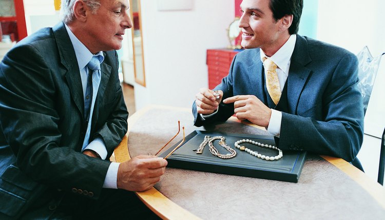 Man Sitting at a Table Opposite a Shop Assistant in a Jewellery Shop Looking at Necklaces and Rings