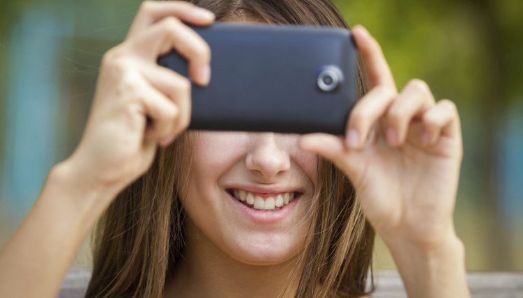 Smiling girl taking photo with smartphone