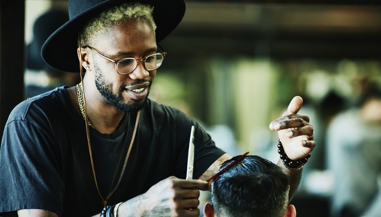 Smiling barber cutting clients hair in barber shop