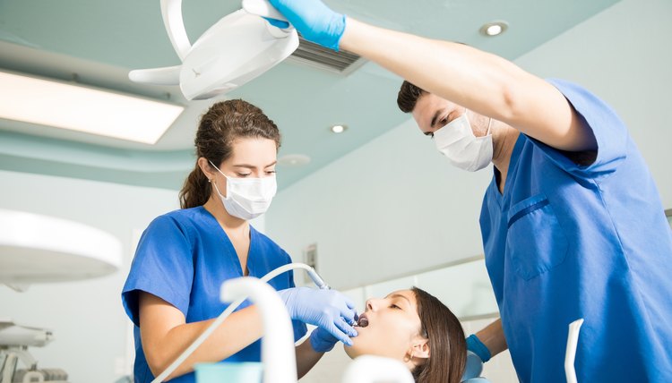 Dentist With Male Colleague Treating Patient At Clinic