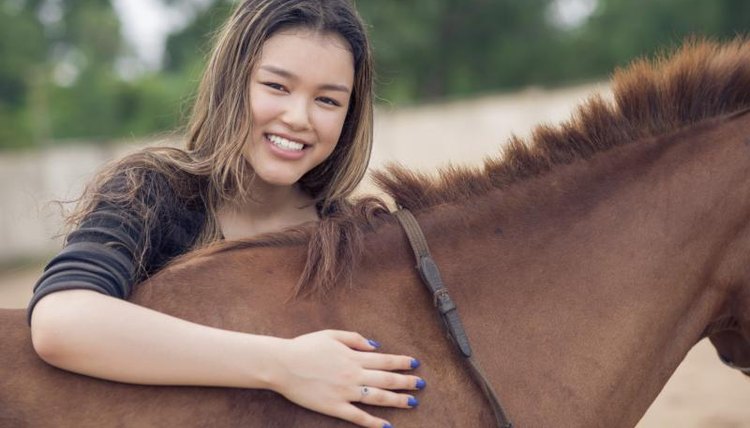 A girl is smiling next to a Bay horse.