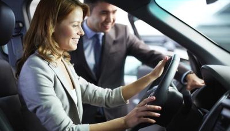 A woman sitting in the driver's seat of a new car with a salesman standing next to her