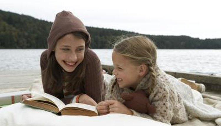 Children reading a book on a lakeside.