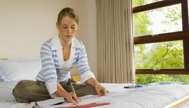 A girl doing homework on her bed.