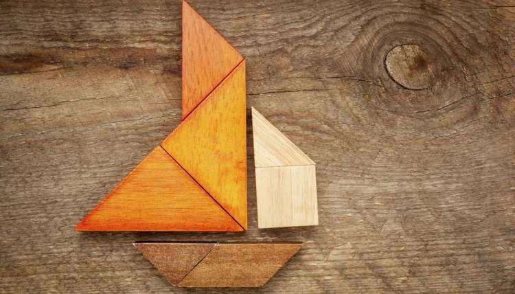 A tangram puzzle in the form of a sailboat, laying on a wooden table.