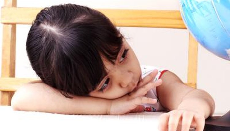 A little girl rests her head on her arm at her desk.