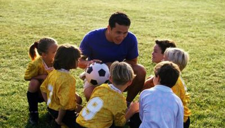 A gym teacher explains the game of soccer to young children on a field.
