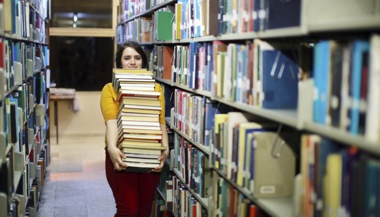 College student carries large stack of books in library