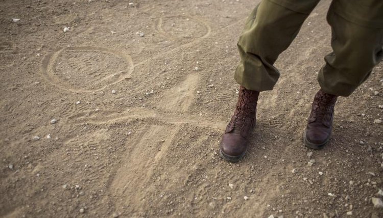 A close-up of a soldier making markings in the dirt with his boot.