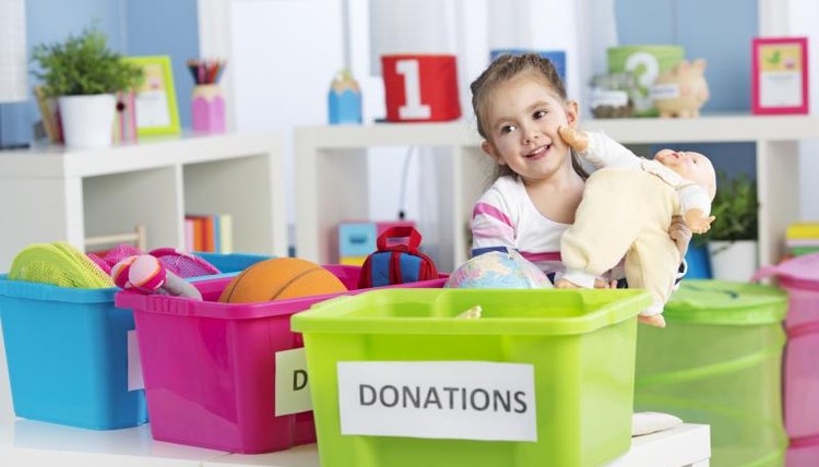 A young girl is bringing a doll to a donation bin at school.