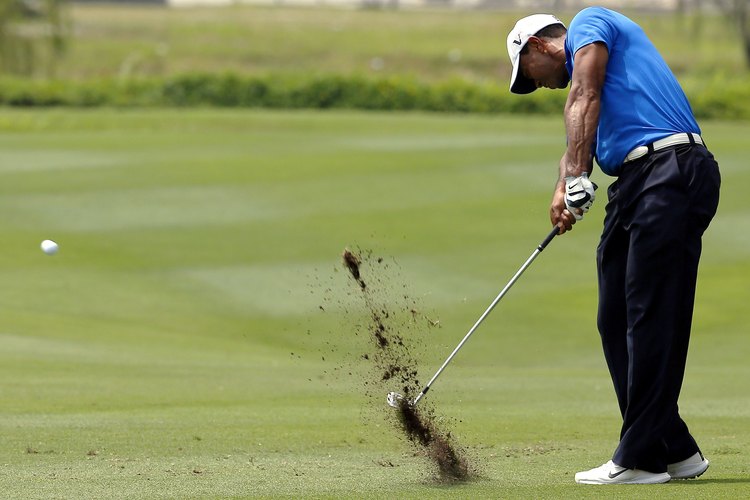 Tiger Woods comprime la pelota, luego realiza un desprendimiento del terreno, utilizando un hierro.