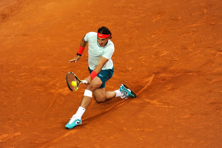 El jugador profesional de tenis Rafa Nadal mantiene su balance mientras devuelve tiros complicados.