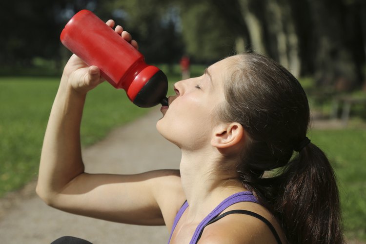 Una mujer bebe de una botella para deportes después de un entrenamiento.