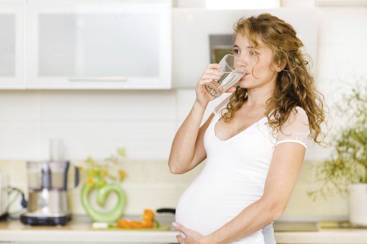Mujer embarazada tomando agua en la cocina.