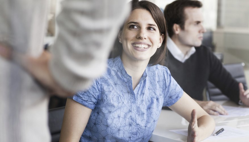 A woman is sitting at a conference table smiling. A woman is sitting at a conference table smiling.
