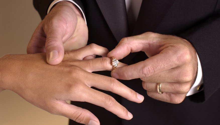 Man putting gold ring on woman's finger Man putting gold ring on woman's finger