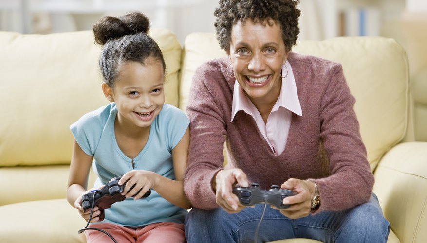 Mother and daughter holding Playstation controllers and sitting on a couch. Mother and daughter holding Playstation controllers and sitting on a couch.