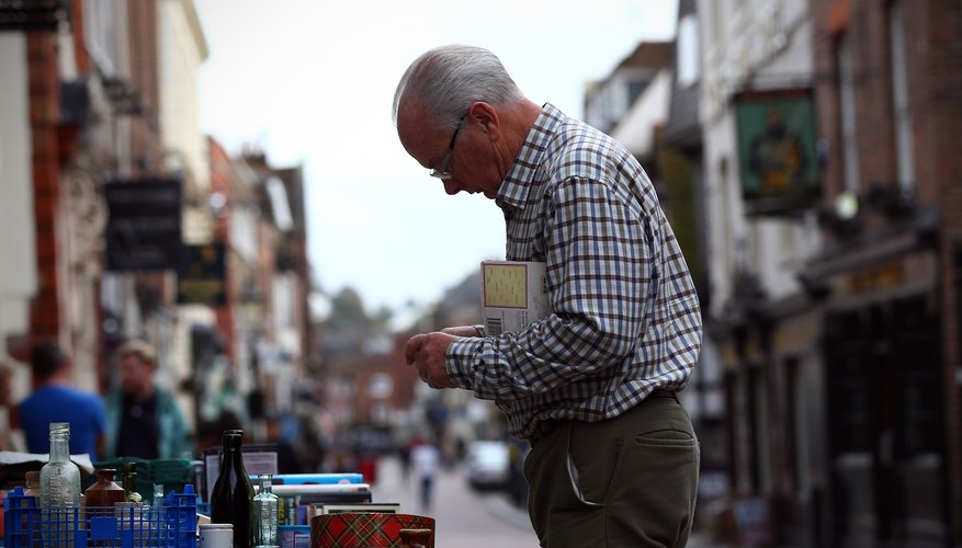 A man inspecting antiques on an outdoor table in town. A man inspecting antiques on an outdoor table in town.