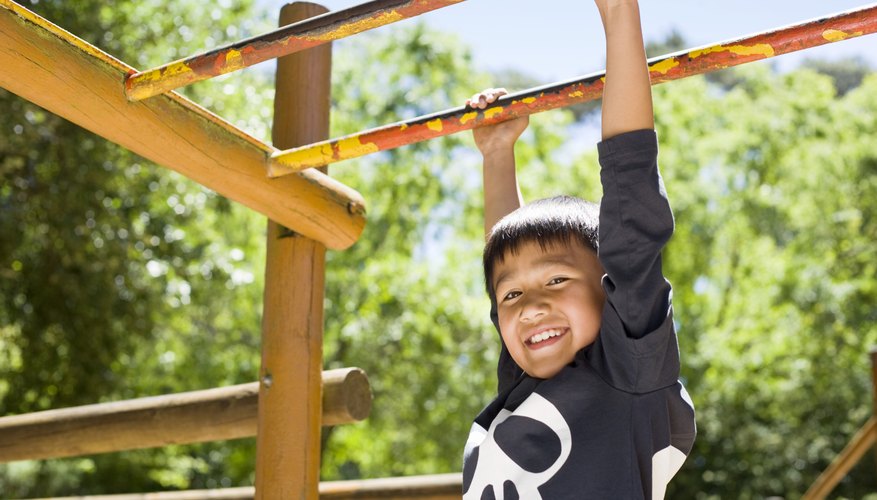 A boy begins climbing across monkey bars. A boy begins climbing across monkey bars.