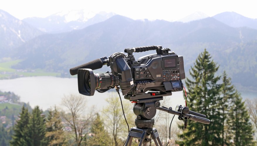 A movie camera is set up on a tripod in an outdoor setting. A movie camera is set up on a tripod in an outdoor setting.