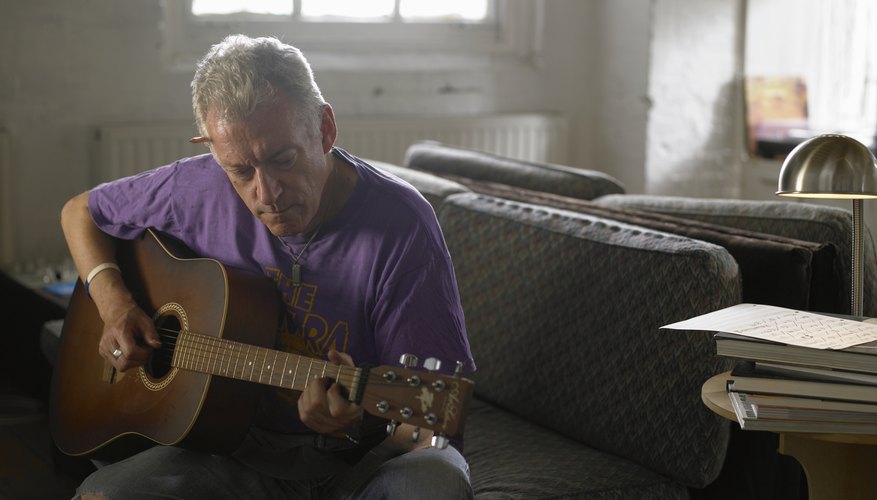Mature man playing an accoustic guitar on a sofa. Mature man playing an accoustic guitar on a sofa.