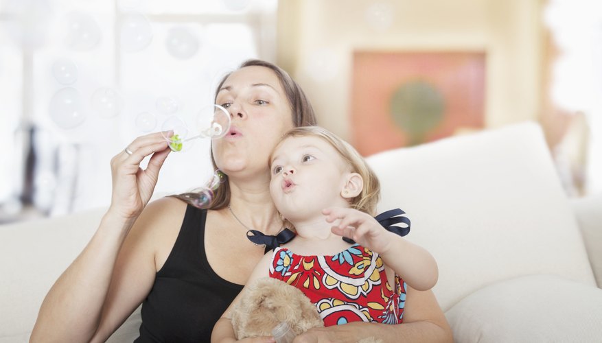Mother blowing bubbles with two year old in her lap. Mother blowing bubbles with two year old in her lap.