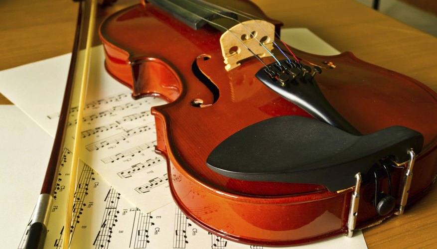 A close-up of a violin, bow and sheet music on a table. A close-up of a violin, bow and sheet music on a table.