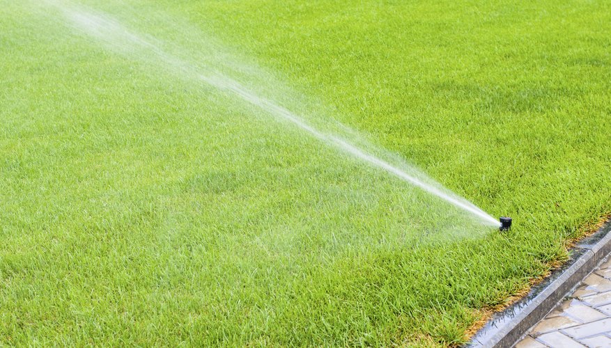A sprinkler irrigating a green lawn with water. A sprinkler irrigating a green lawn with water.