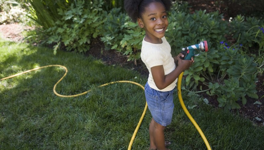 A young girl waters the yard with a hose. A young girl waters the yard with a hose.