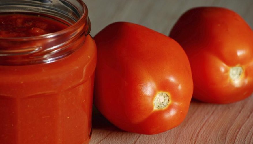 Plum tomatoes on a cutting board next to a jar of homemade tomato sauce. Plum tomatoes on a cutting board next to a jar of homemade tomato sauce.