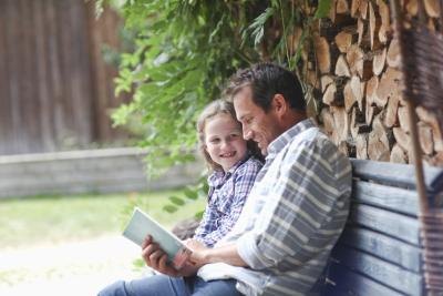 A father shares a book with his daughter on a bench at a cabin.