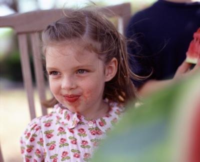 A little girl has red fruit on her chin.
