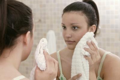A woman looks in the mirror and dries her face with a towel.