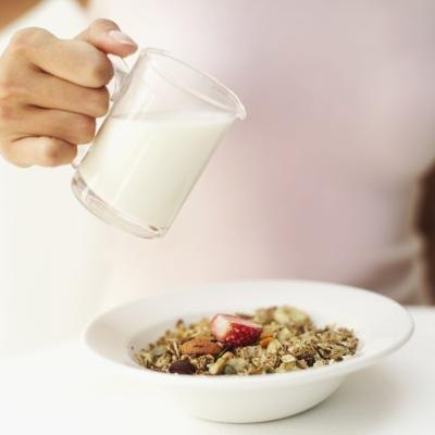 A woman pours skim milk over cereal.