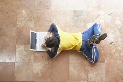 A high angle view of a boy looking at a laptop on the floor.