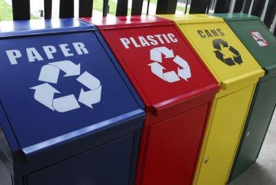 Four colorful recycling bins lined up by category outside.