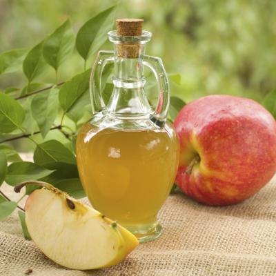 A bottle of apple cider vinegar on a table with apples