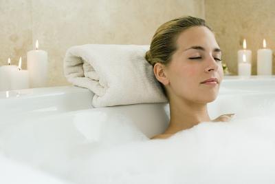 A woman relaxes in a bubble bath surrounded by lit candles.